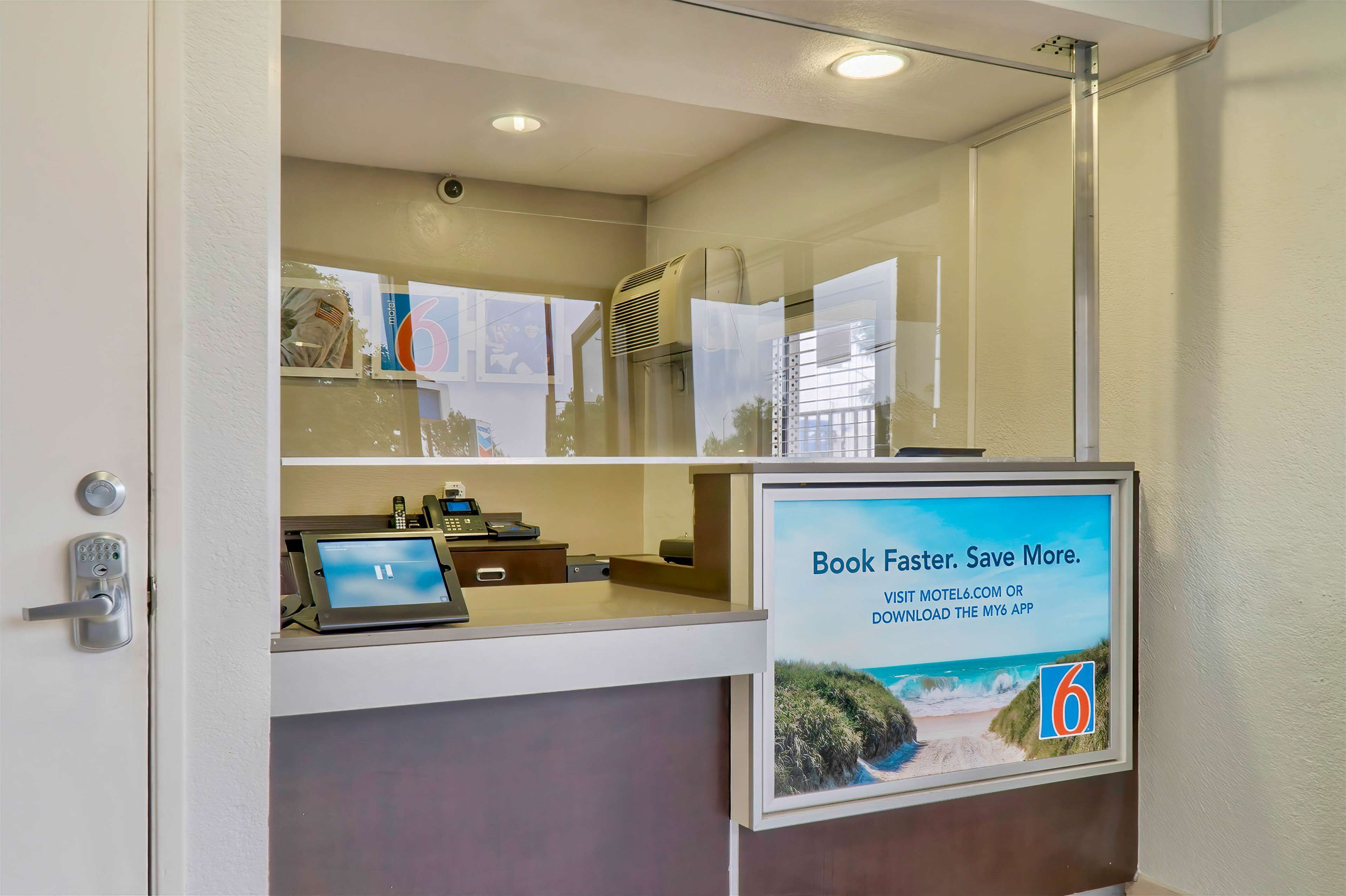 A reception desk with a digital screen, a phone, and a poster advertising a website and app.