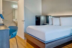 Una habitación de hotel moderna con cama, mesitas de noche, escritorio, silla y baño visible a través de una puerta abierta.