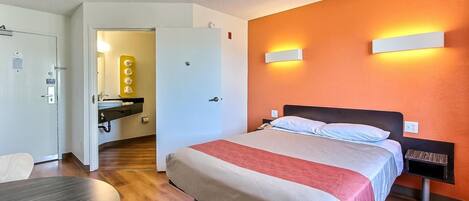 Una habitación de hotel con cama, mesita de noche y escritorio con silla.