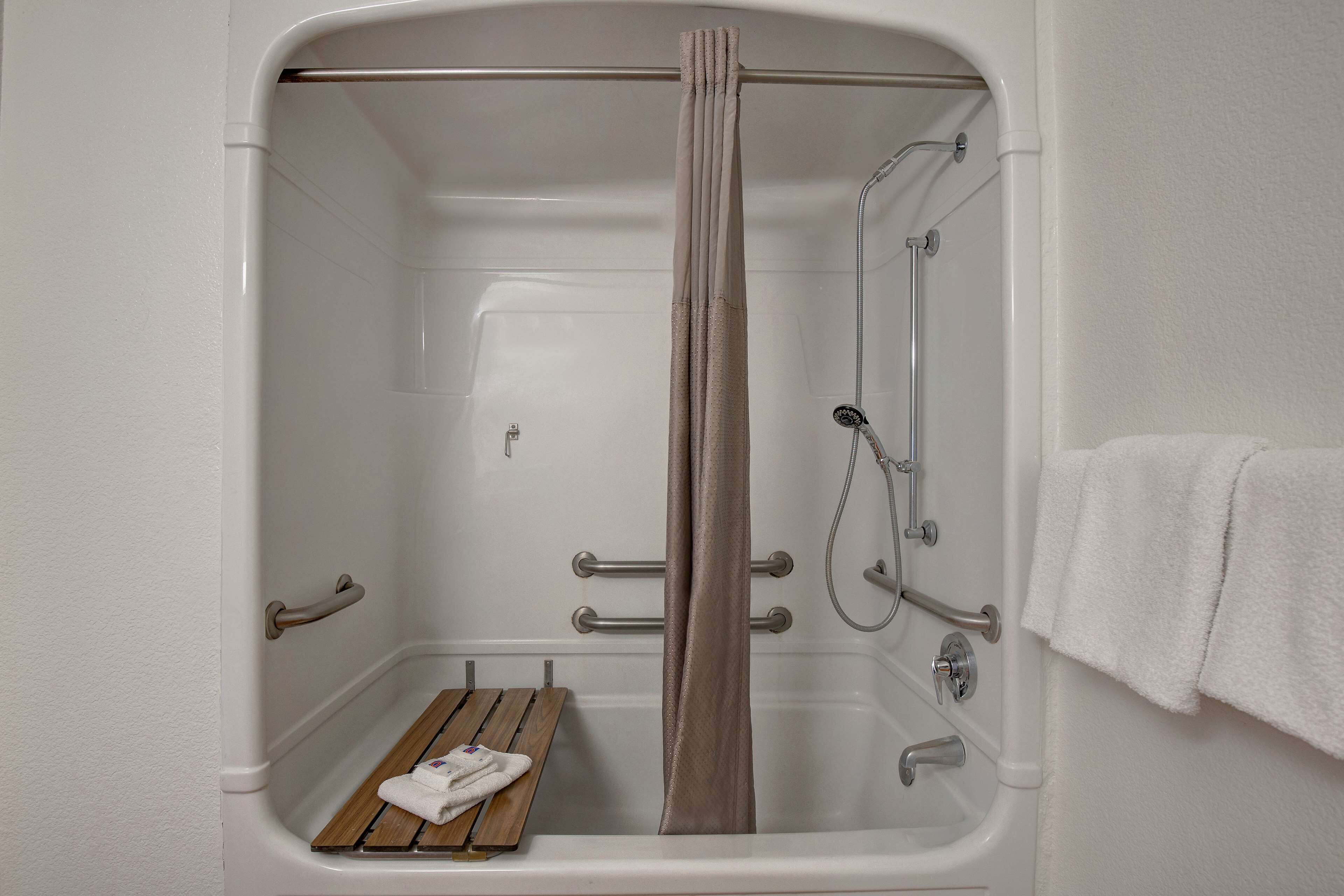 Eine Dusche ohne trittstufen mit einer hölzernen Sitzbank, Haltegriffen und einem Handtuchhalter.