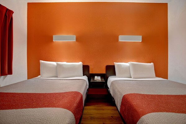 Quarto de hotel com duas camas, piso de madeira e cortina vermelha.