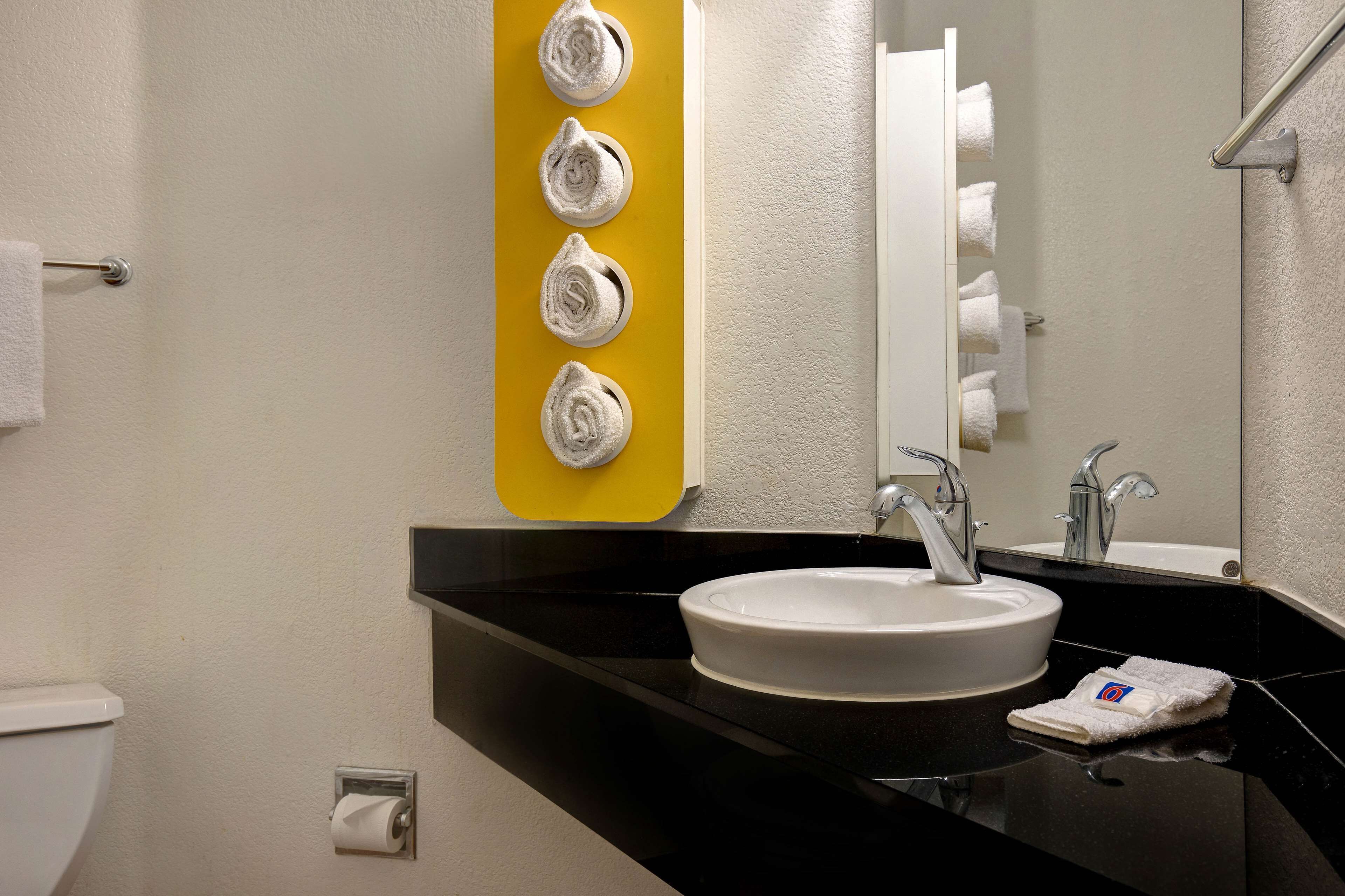 A bathroom with a white sink, black countertop, and a yellow towel rack with towels.
