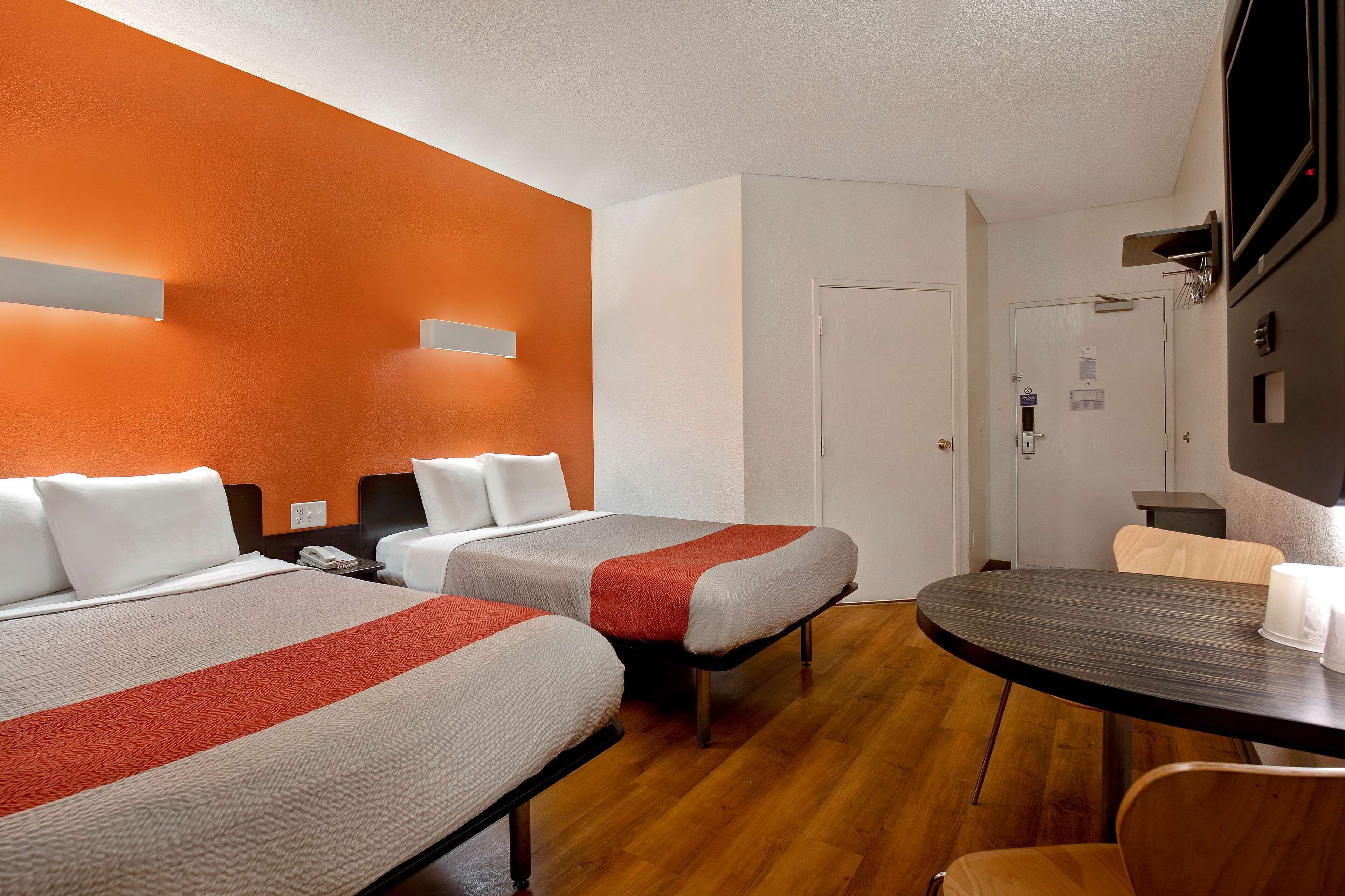 A hotel room with two beds, a wooden floor, a round table, and a white door.