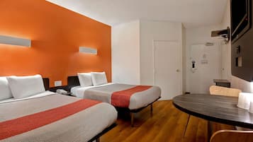 A hotel room with two beds, a wooden floor, a round table, and a white door.