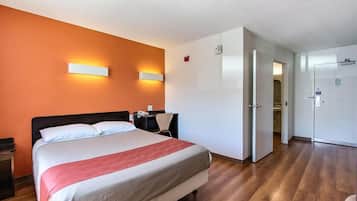A hotel room with a large bed, a desk, and a chair. There is a door leading to another room.