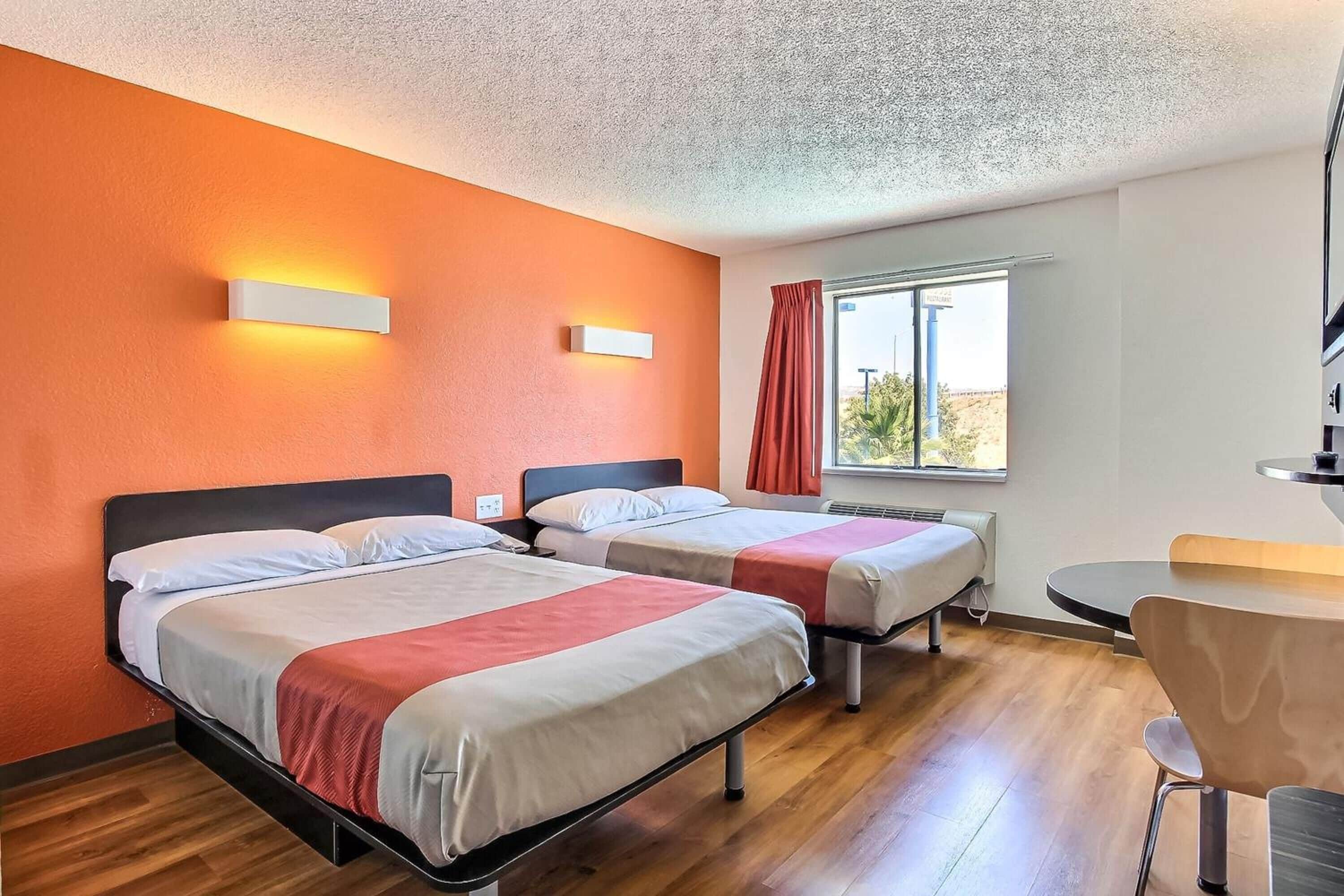 A hotel room with two beds, a desk, and a window with curtains.