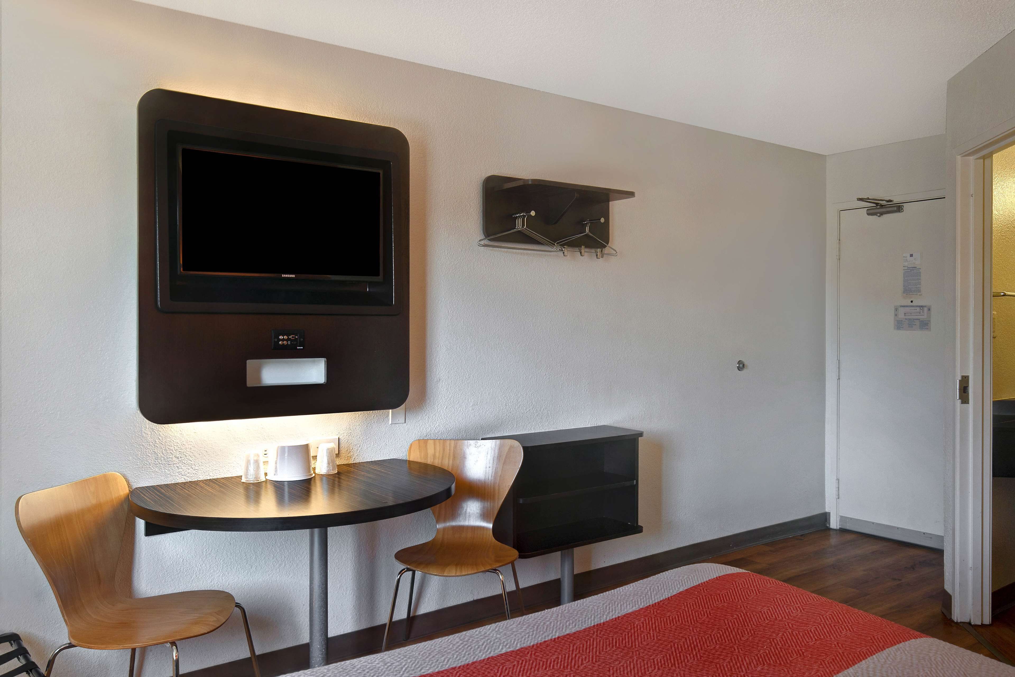 A modern room with a flat-screen TV mounted on the wall, a small table with two chairs, and a coat rack with hangers.