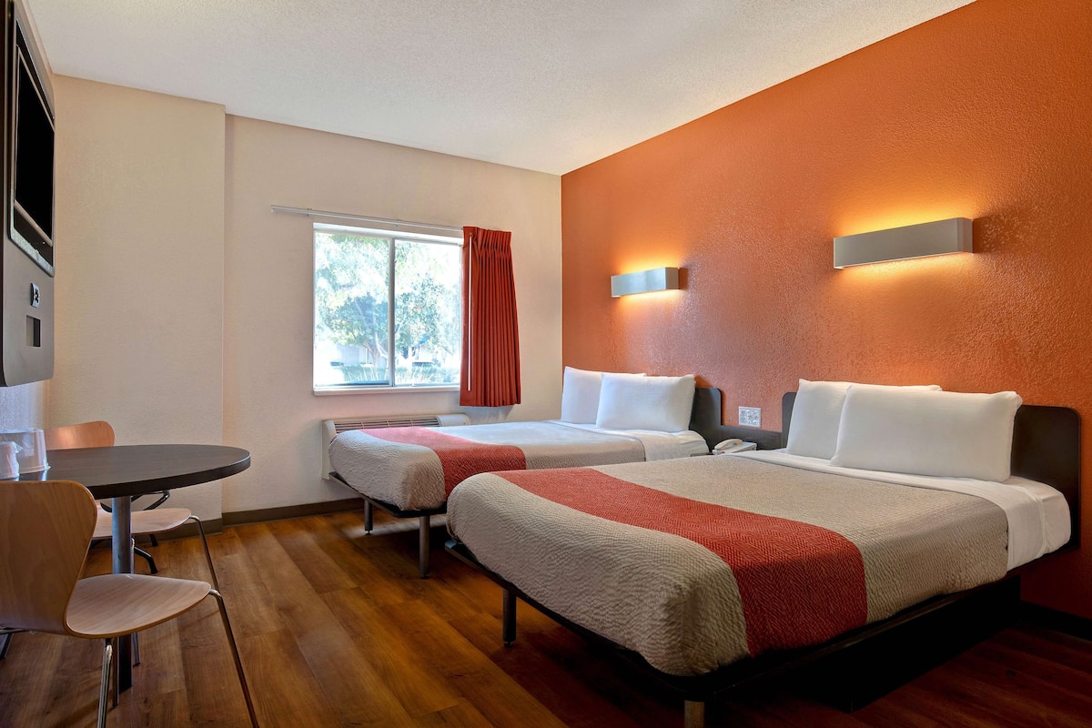 Habitación de hotel con dos camas, una mesa de comedor y una ventana con cortinas.