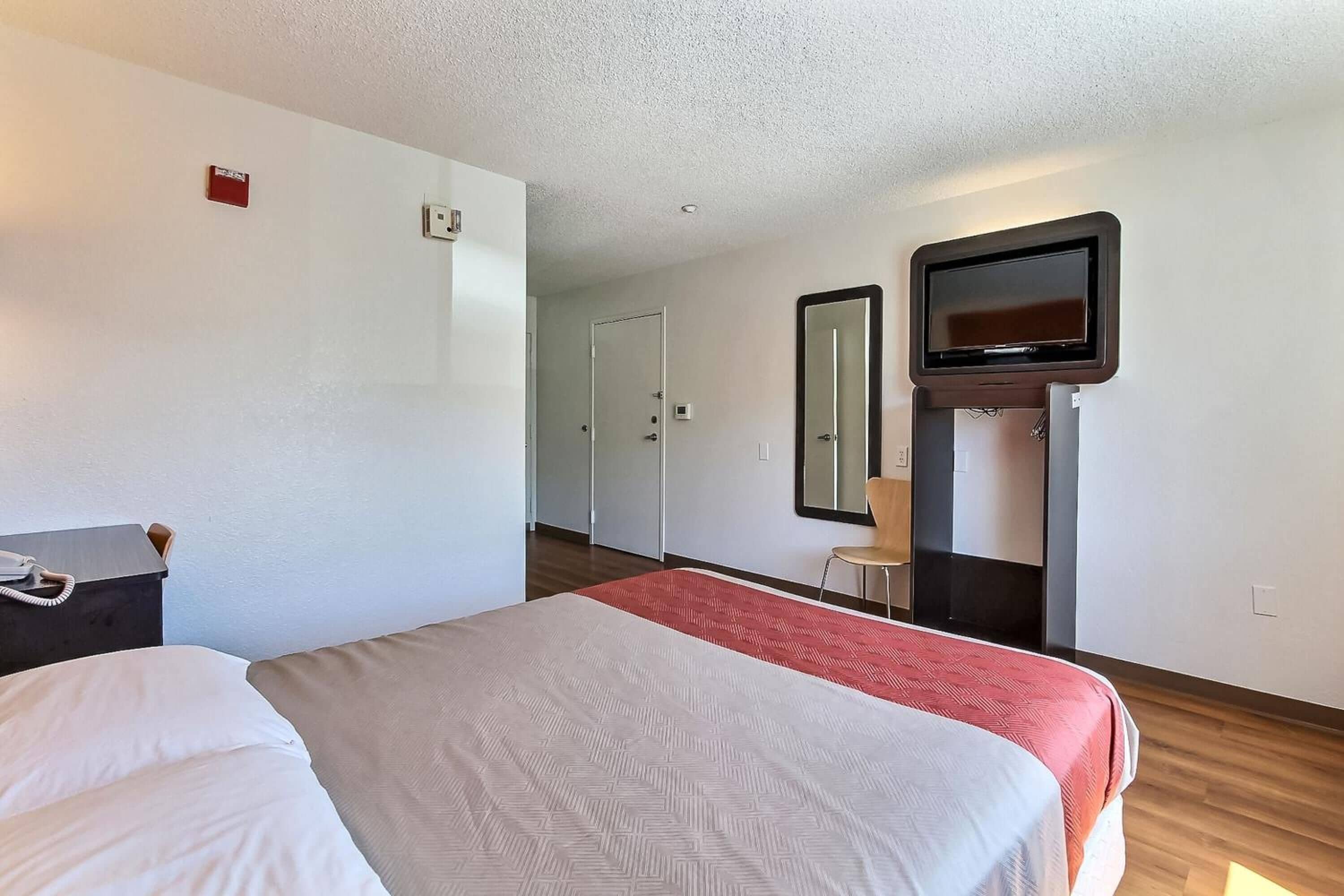 A hotel room with a bed, a TV mounted on the wall, a desk with a phone, and a door leading to a closet.
