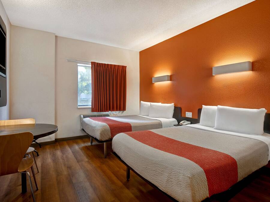 Quarto de hotel com duas camas, uma escrivaninha e uma janela com cortinas.