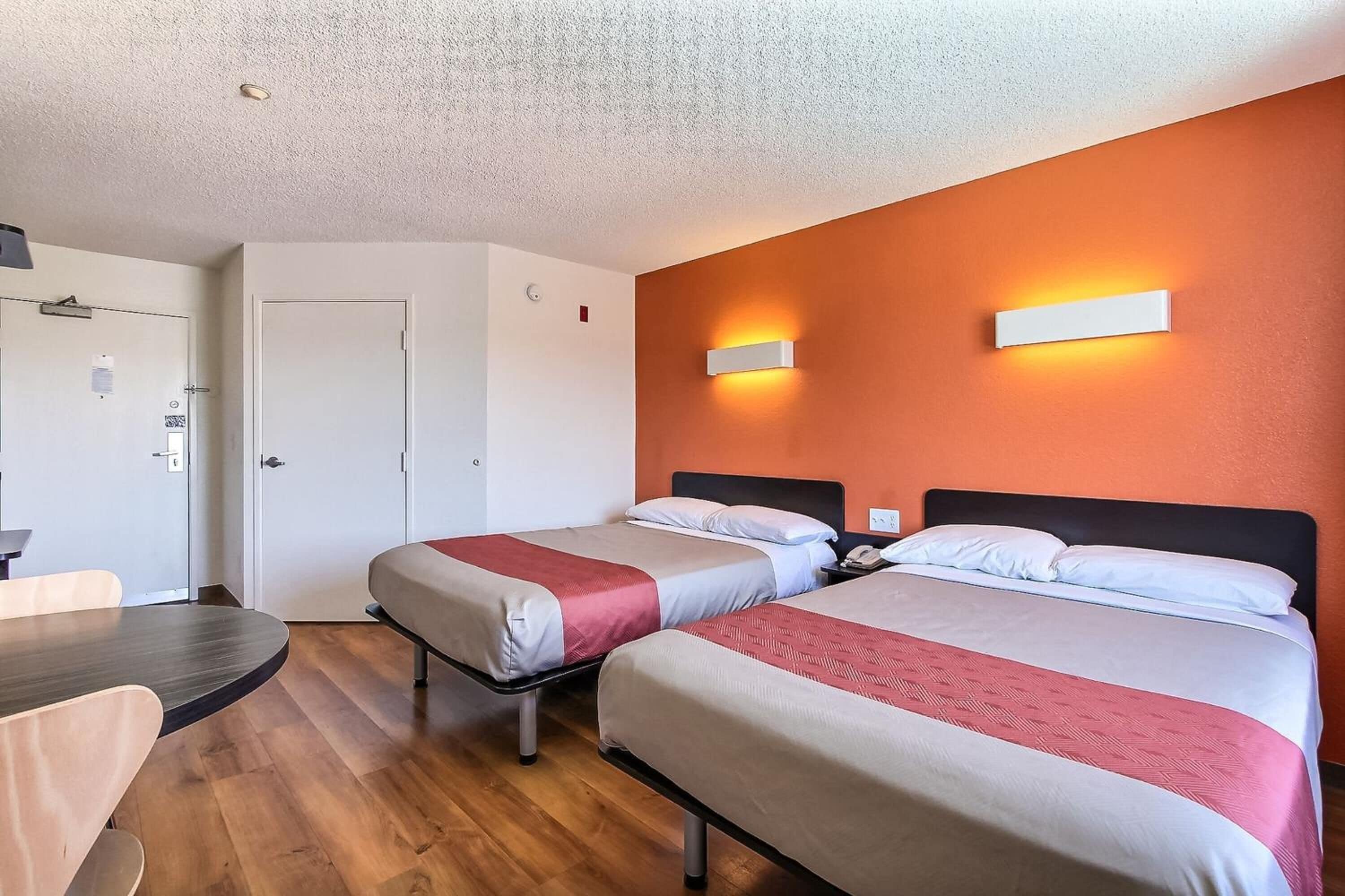 A hotel room with two beds, a desk, and a door.