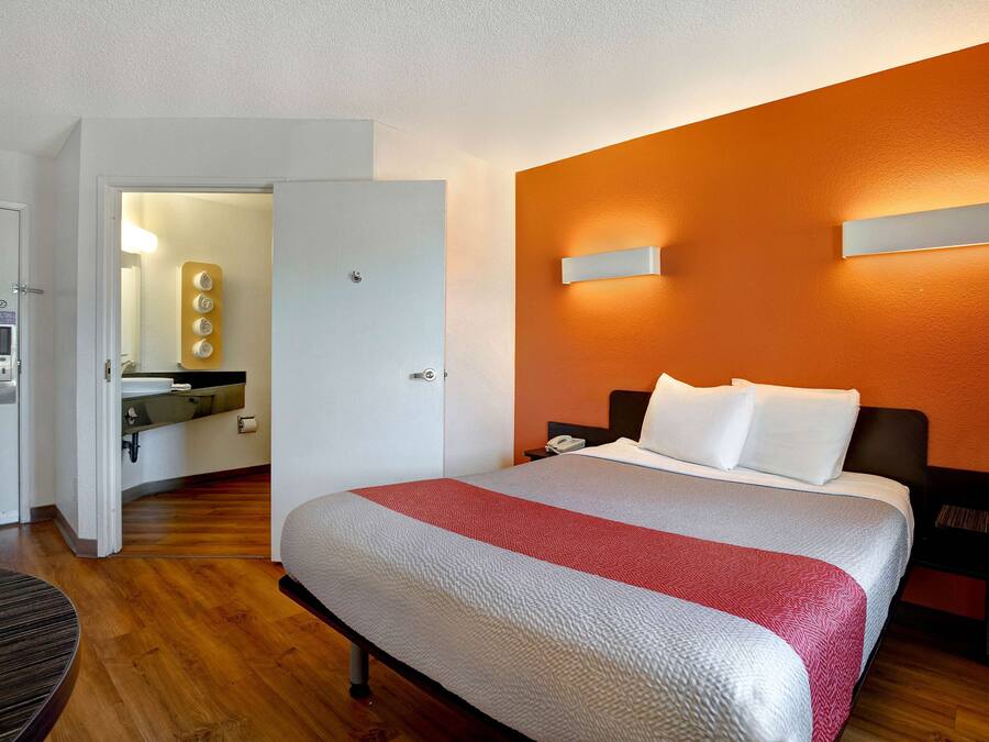 Camera d'albergo con un letto, un comodino, uno specchio e un bagno visibile attraverso una porta aperta.