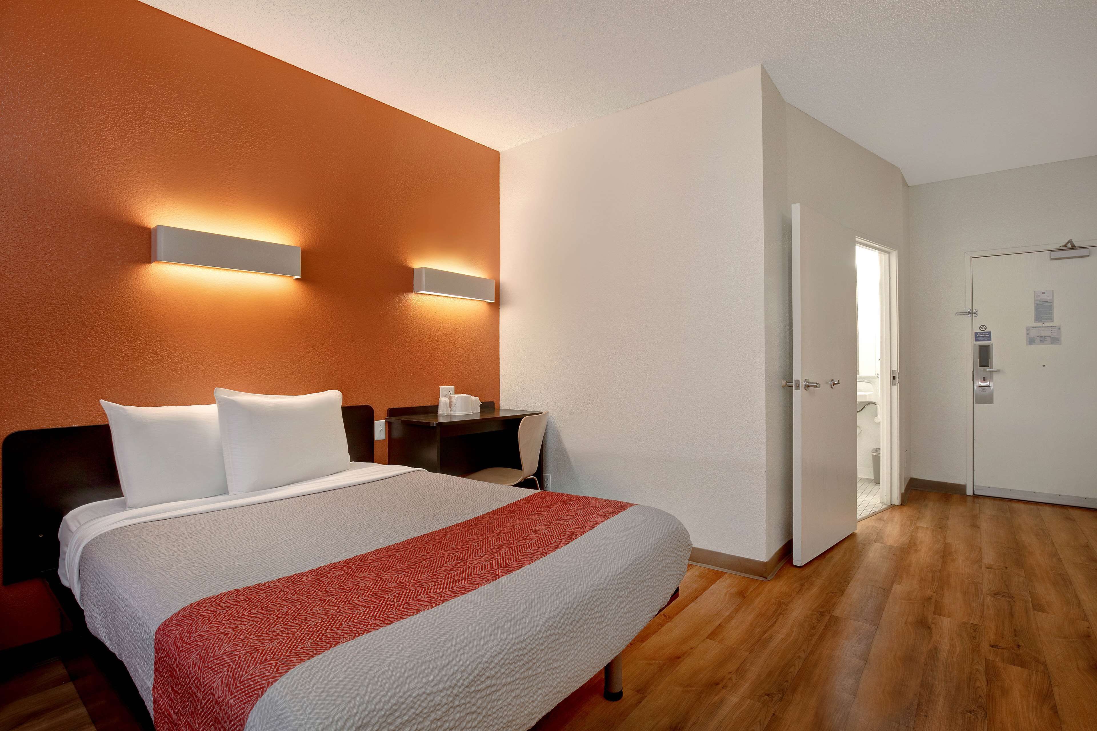 A hotel room with a large bed, a nightstand, a desk, and a door leading to a bathroom.