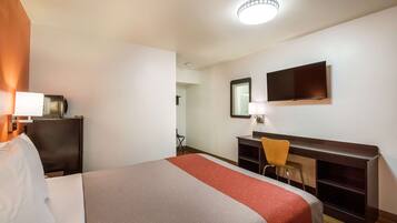 A hotel room with a bed, a desk, a chair, a television, and a mirror.