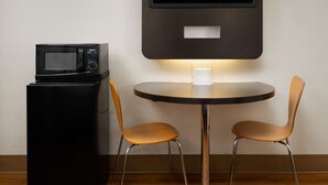 Eine kompakte Küchenzeile mit Mikrowelle, kleinem Kühlschrank und einem Tisch mit zwei Stühlen.