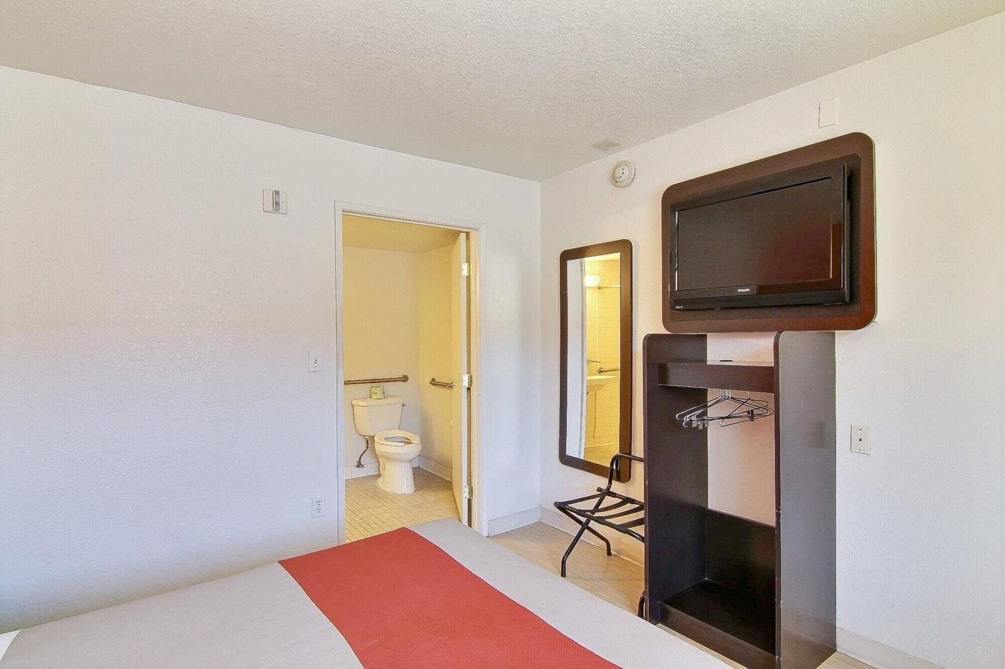 Habitación de hotel con cama, televisión montada en la pared, espejo y puerta que da a un baño.