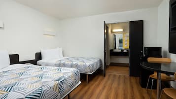 A hotel room with two beds, a desk, and a bathroom visible through an open door.