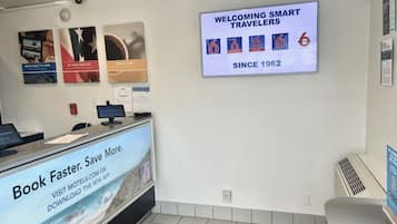 Una mesa de recepción con una pantalla digital que muestra un mensaje de bienvenida para viajeros inteligentes y un cartel que promociona una aplicación de reservas.