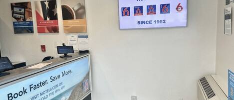 A reception desk with a digital screen displaying a welcome message for smart travelers and a sign promoting a booking app.