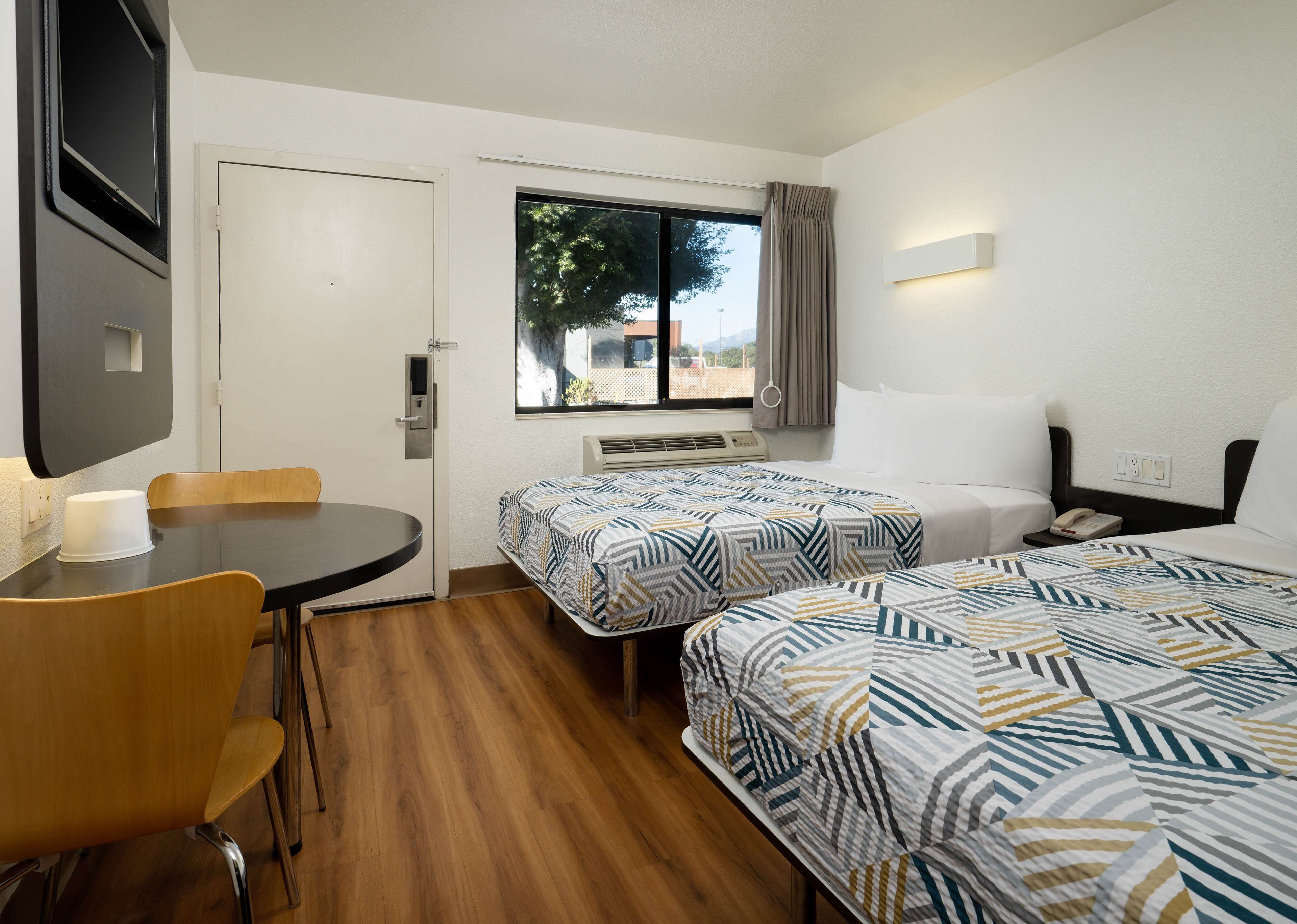 A hotel room with two beds, a desk, a chair, a window with a view, and a TV mounted on the wall.
