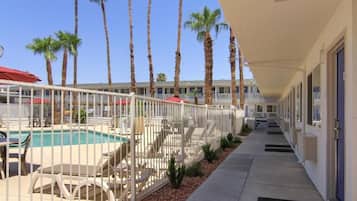 A hotel with a pool area, palm trees, and a covered walkway.