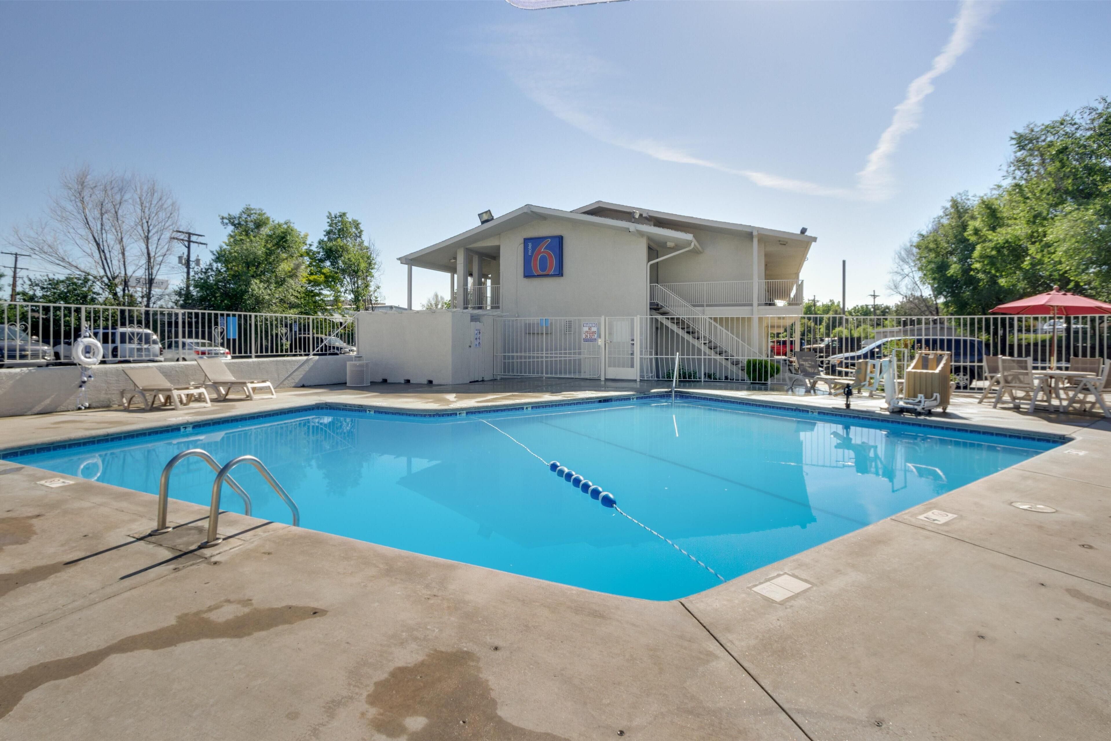 Una piscina con zona vallada, un edificio con un letrero que dice '6' y mobiliario exterior.