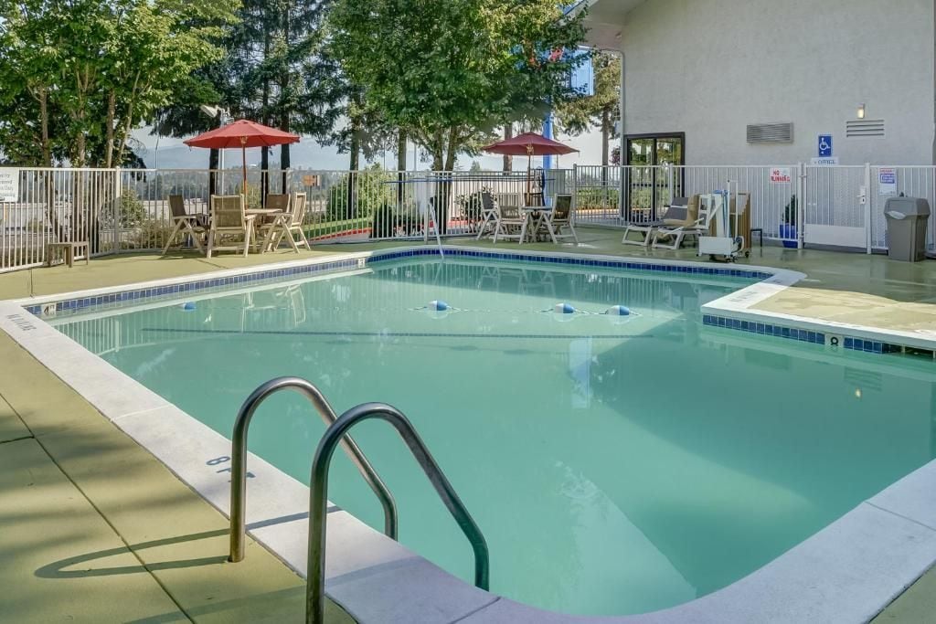 Una piscina con una escalera metálica, sillas de descanso y sombrillas.