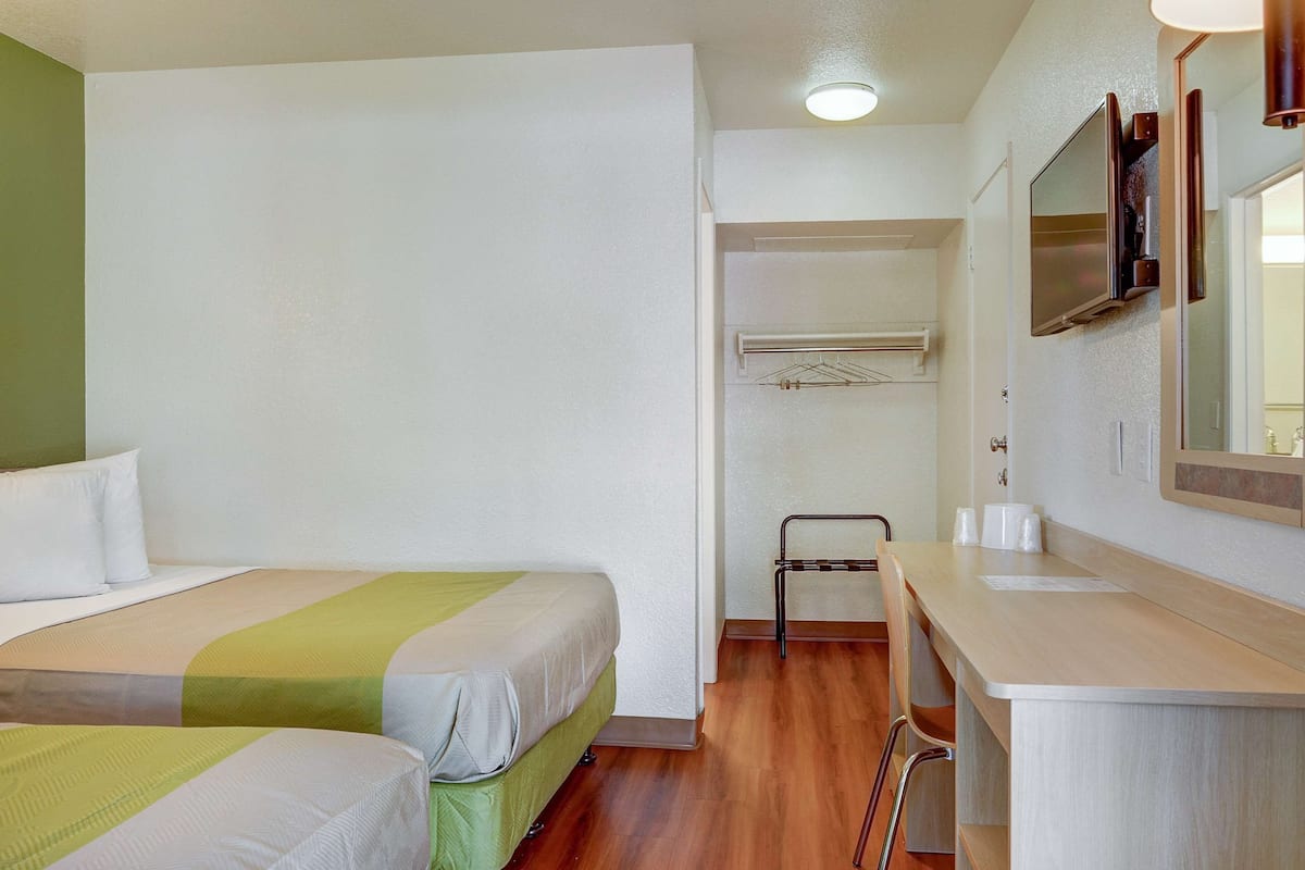 A hotel room with two beds, a small bathroom, and a wooden floor.