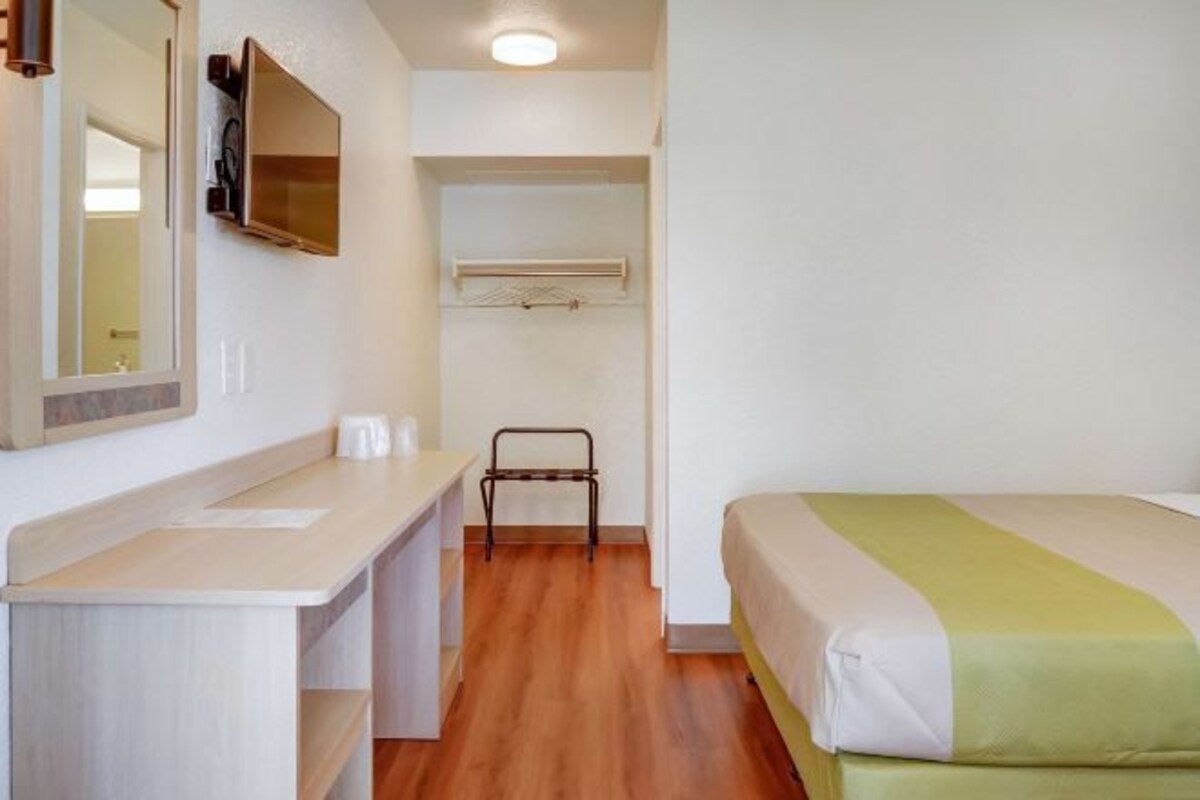 A small, clean room with a bed, a desk, a mirror, and a television.