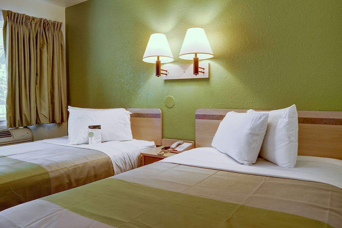 A hotel room with two beds, a bedside table with a phone, and wall-mounted lamps.