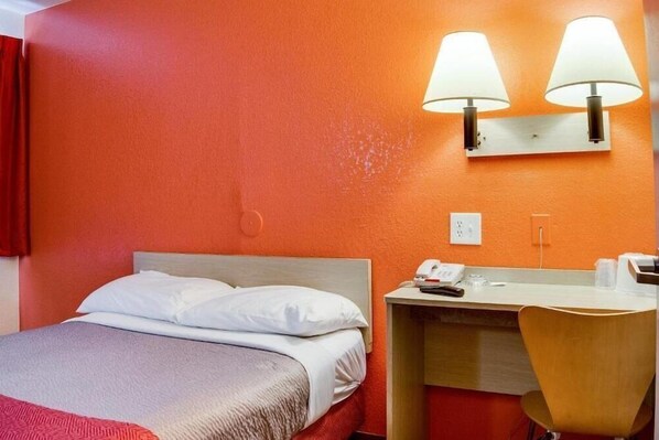 A hotel room with a bed, a desk, and two wall-mounted lamps. - Motel 6 Kelso - Mt. St. Helens (Kelso)