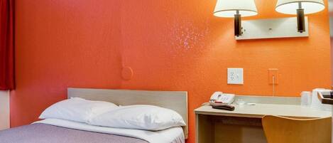 Une chambre d’hôtel équipée d’un lit, d’un bureau, d’une chaise et de deux lampes fixées au mur.
