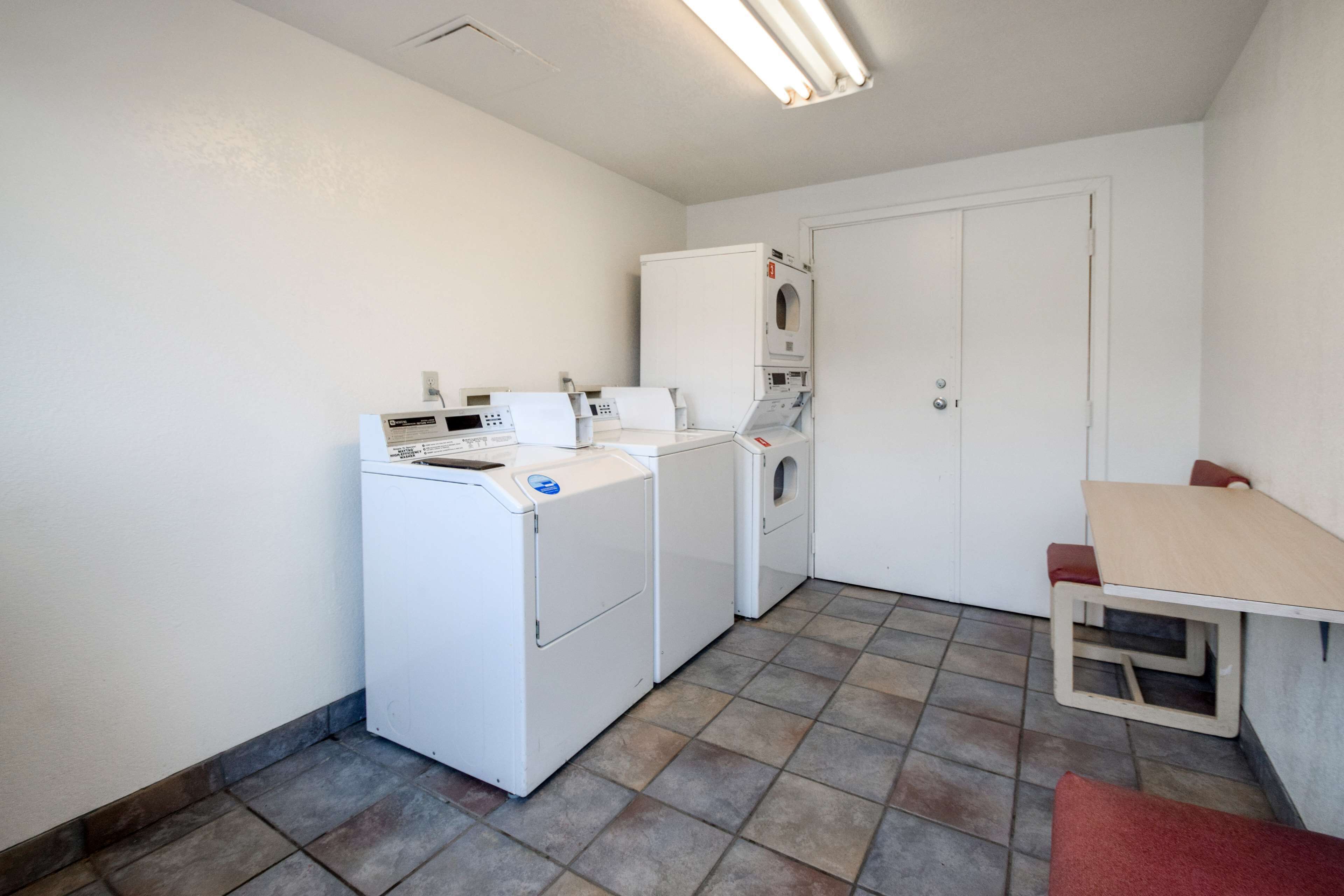 A compact laundry room with a washing machine, dryer, and a small table with a bench.