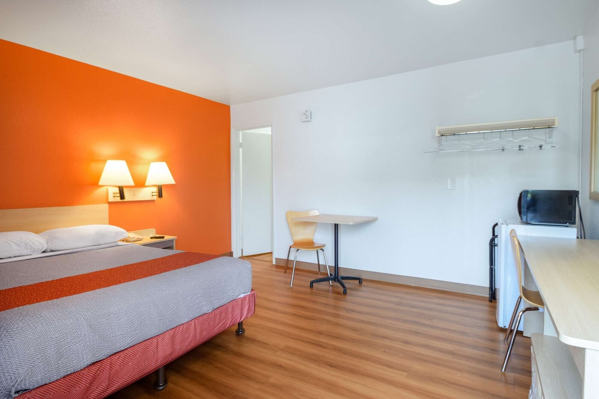 Une chambre d’hôtel avec un lit, un bureau et une chaise. Deux lampes sont fixées au mur de chaque côté du lit.
