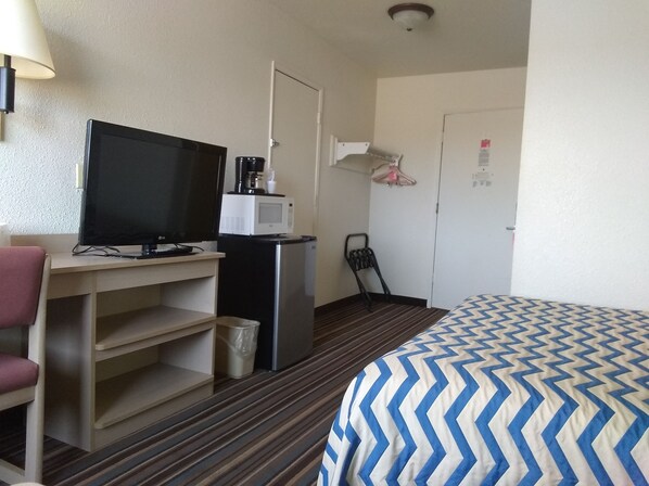 A hotel room with a bed, a desk with a television, a refrigerator, and a trash bin. - Sioux City Inn (Sioux City)