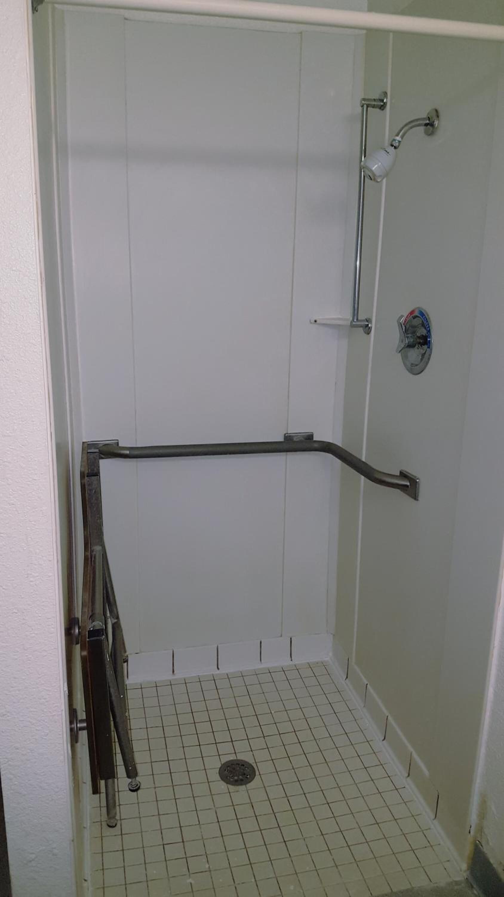A small, enclosed shower area with a metal grab bar, a showerhead, and a tiled floor.