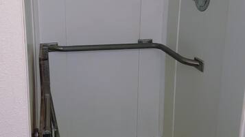 A small, enclosed shower area with a metal grab bar, a showerhead, and a tiled floor.