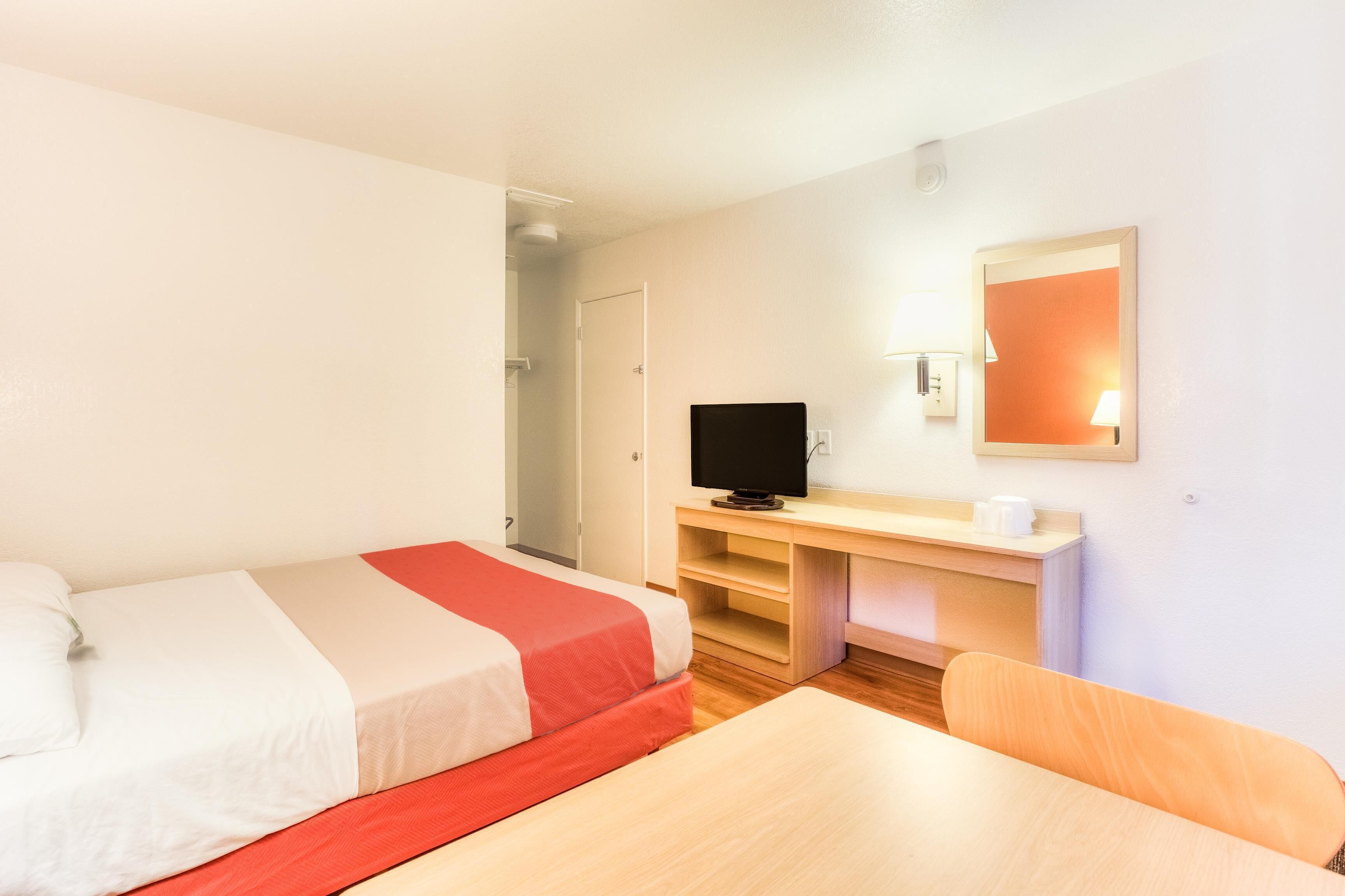 Una habitación de hotel con cama, escritorio, silla, televisión y espejo.