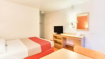 Una habitación de hotel con cama, escritorio, silla, televisión y espejo.