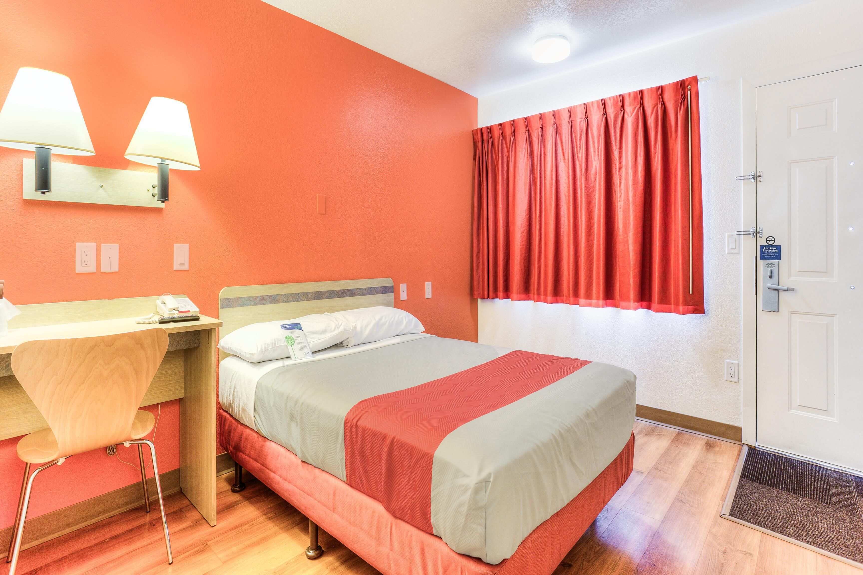 A hotel room with a bed, desk, chair, and a window with curtains.