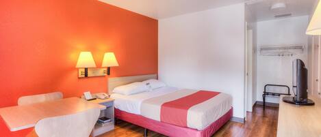 A hotel room with a bed, a desk, a chair, a TV, and a lamp.