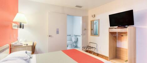 A hotel room with a bed, a desk with a lamp, a television, and a walk-in closet.