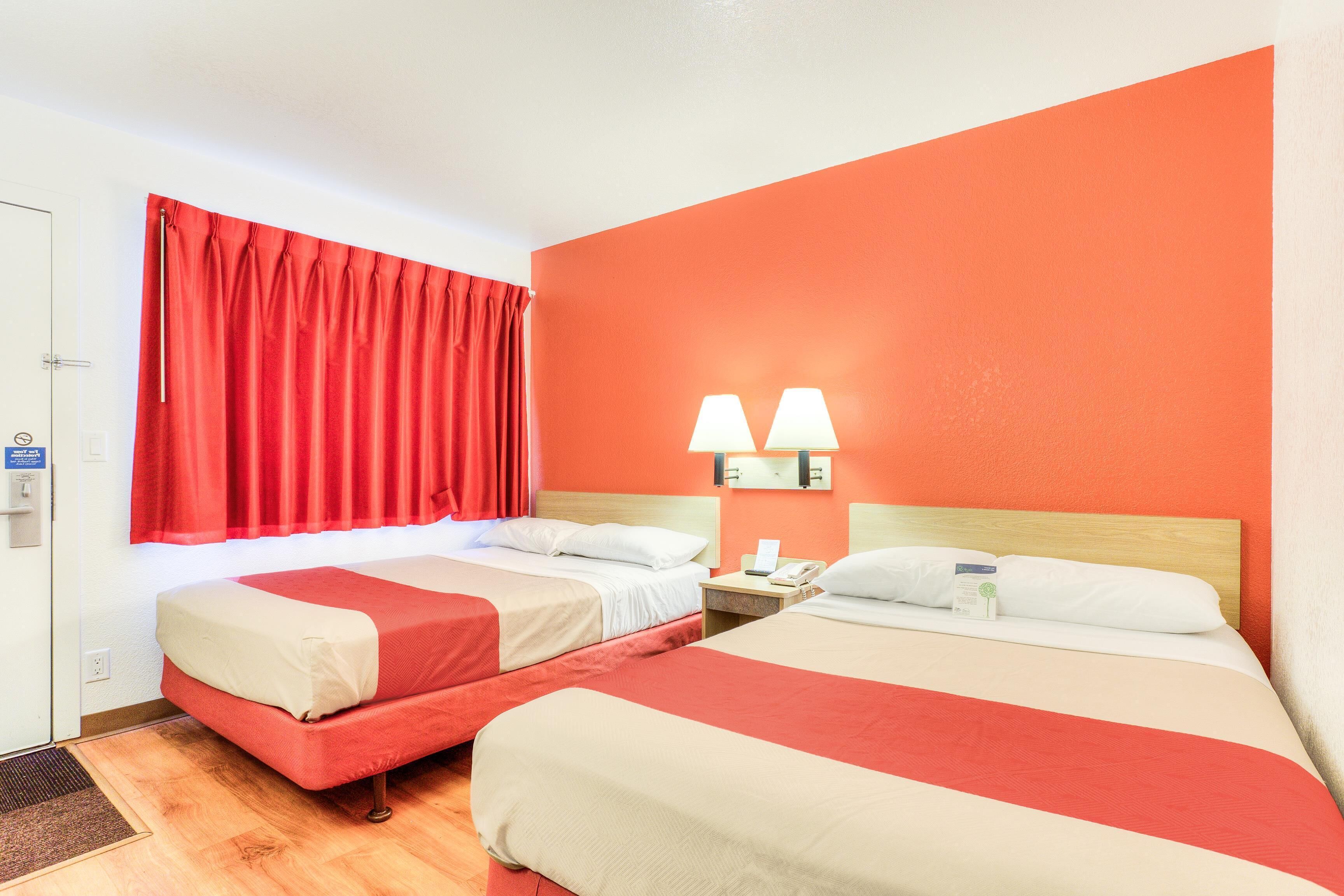 A hotel room with two beds, a red curtain, and two wall-mounted lamps.