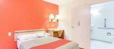 Ein Hotelzimmer mit Bett, Schreibtisch, Stuhl, Nachttisch und einem Badezimmer mit Dusche und Toilette.