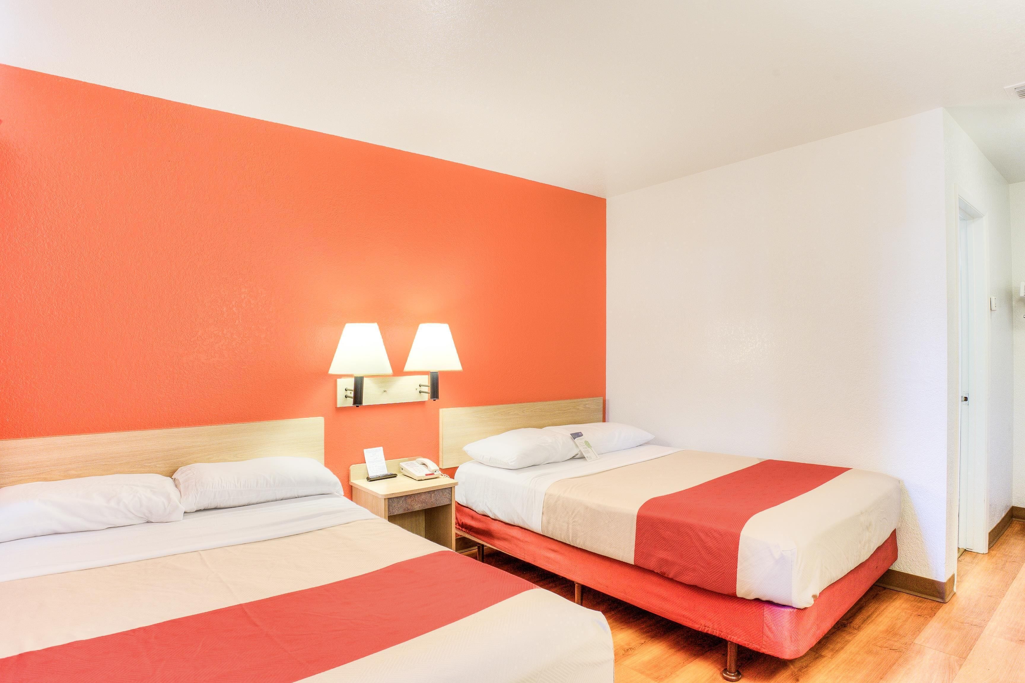 A hotel room with two beds, a wooden headboard, a nightstand with a lamp, and a phone.
