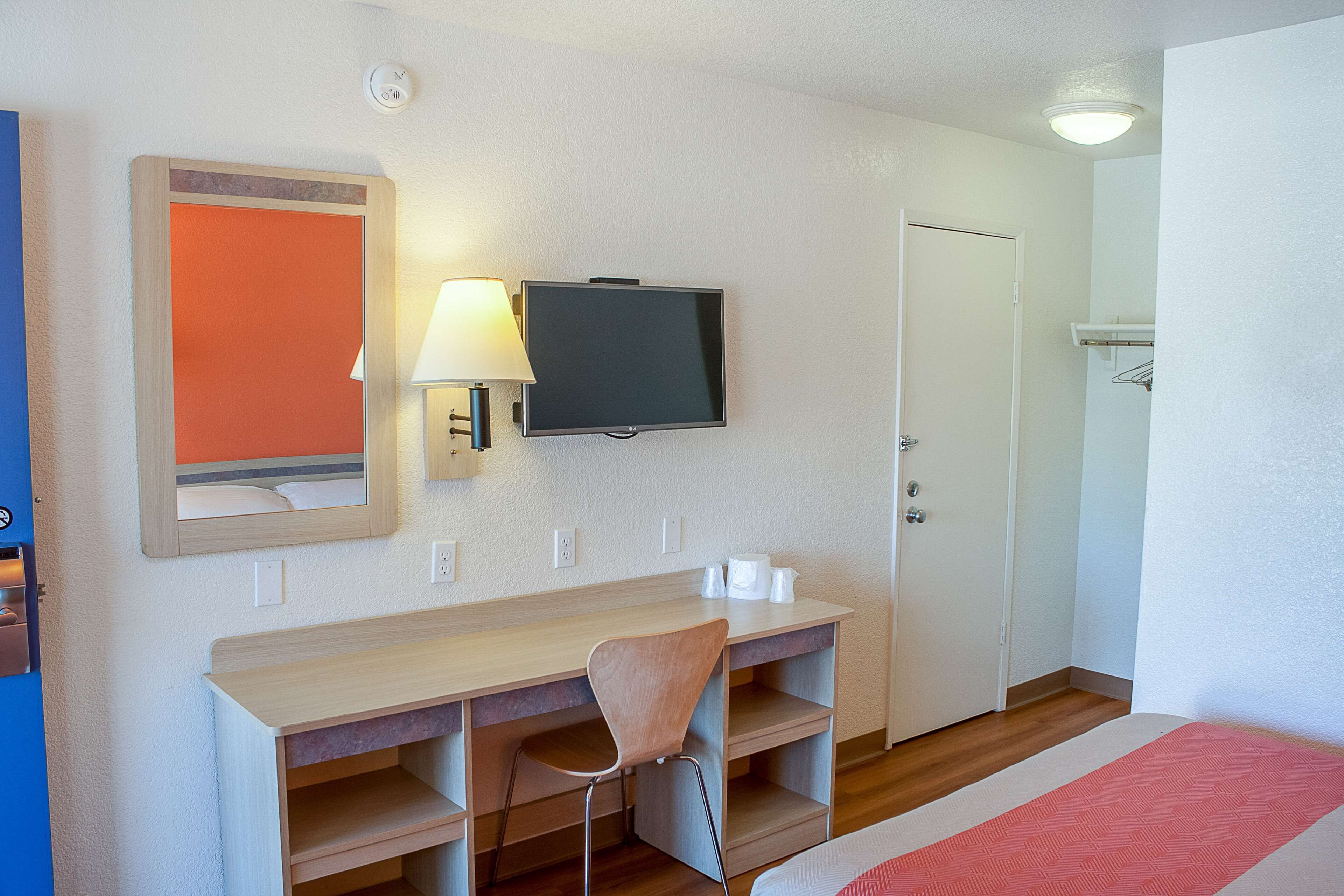 A hotel room with a wooden desk, a chair, a television, and a bed.