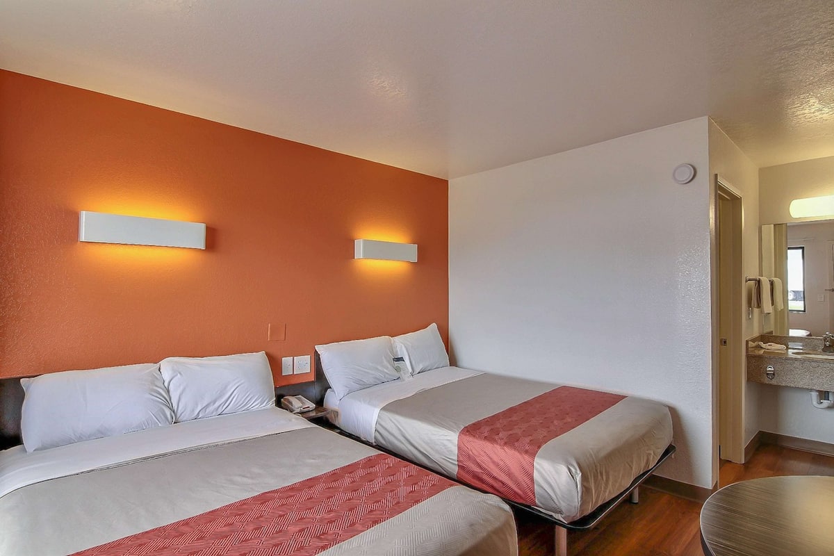 A hotel room with two beds, a bathroom with a mirror and sink, and a small table.