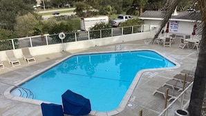 Una piscina rectangular con un borde de baldosas, rodeada de sillas de descanso y una valla.