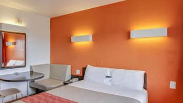 Quarto de hotel com uma cama, uma mesa e uma cadeira. Há duas luminárias fixadas na parede.