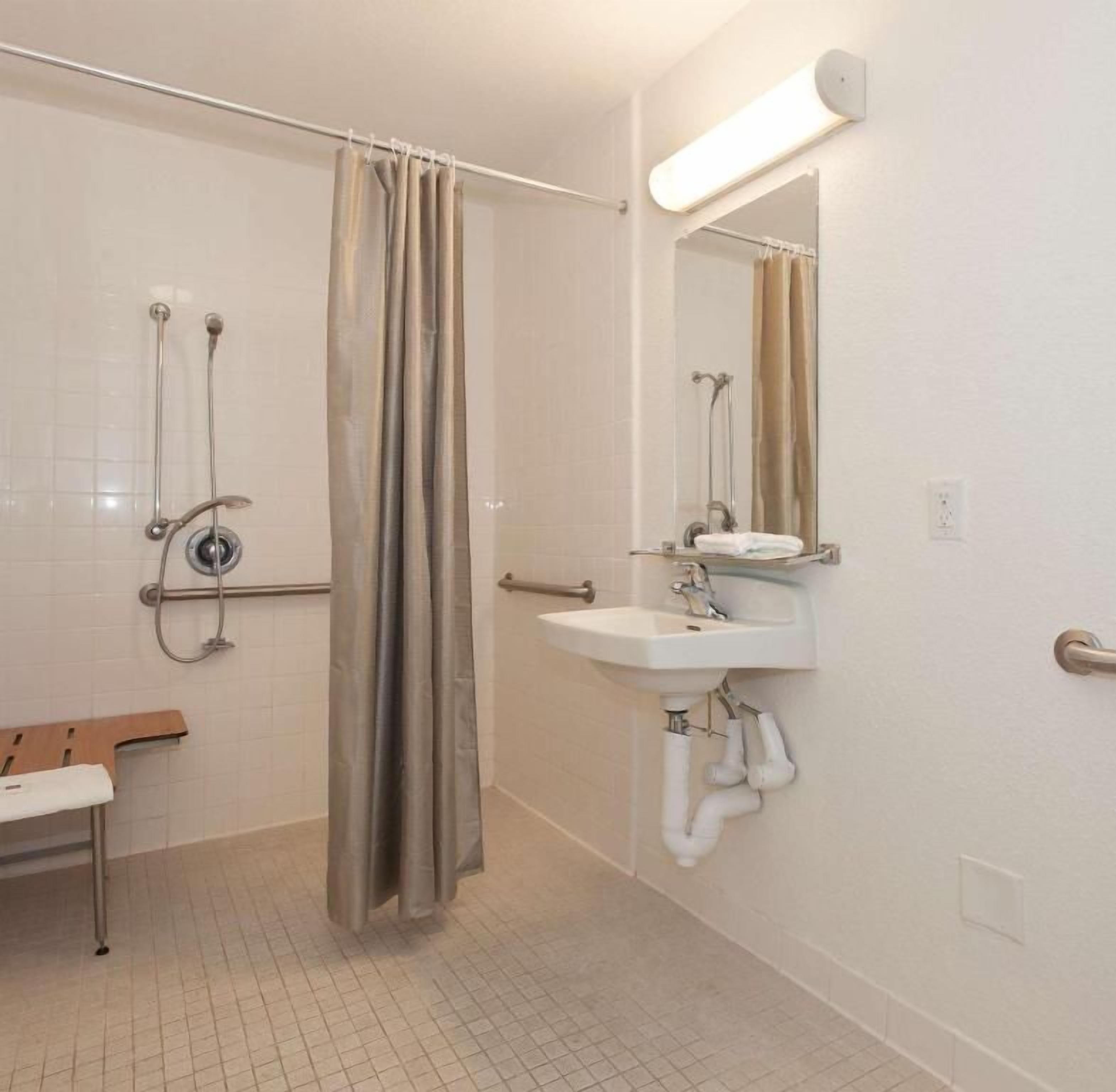 Un baño con ducha, lavamanos, banco y espejo.